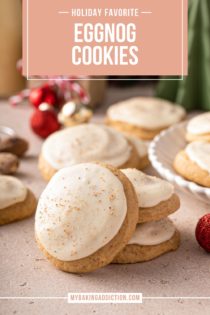 Two stacked eggnog cookies with a third leaning against the stack. More cookies are visible in the background. Text overlay includes recipe name.