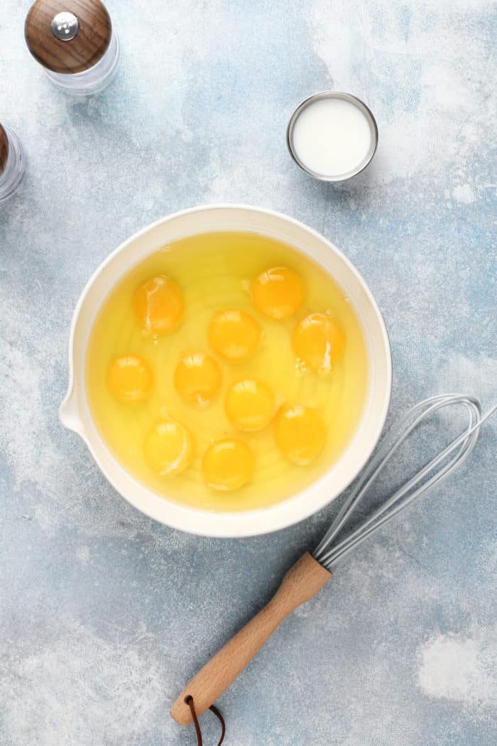 Eggs cracked into a white mixing bowl next to a small bowl of milk.