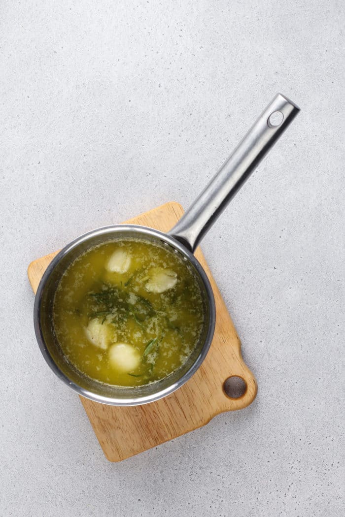 Garlic herb butter in a small saucepan set on a wooden trivet.