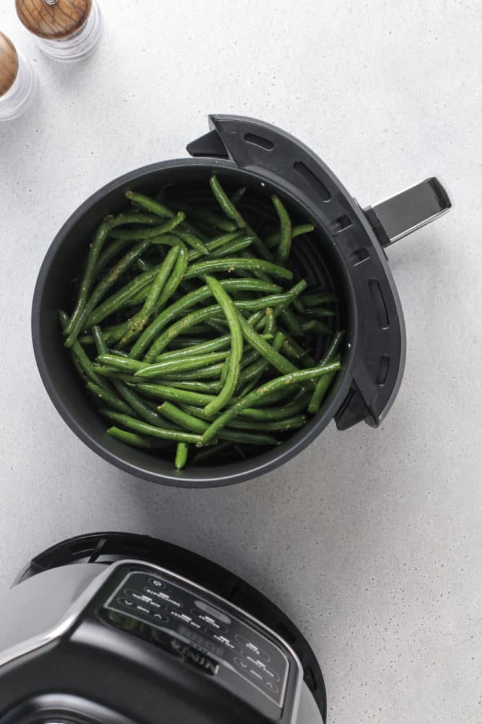 Cooked green beans in the basket of an air fryer set on a gray countertop.