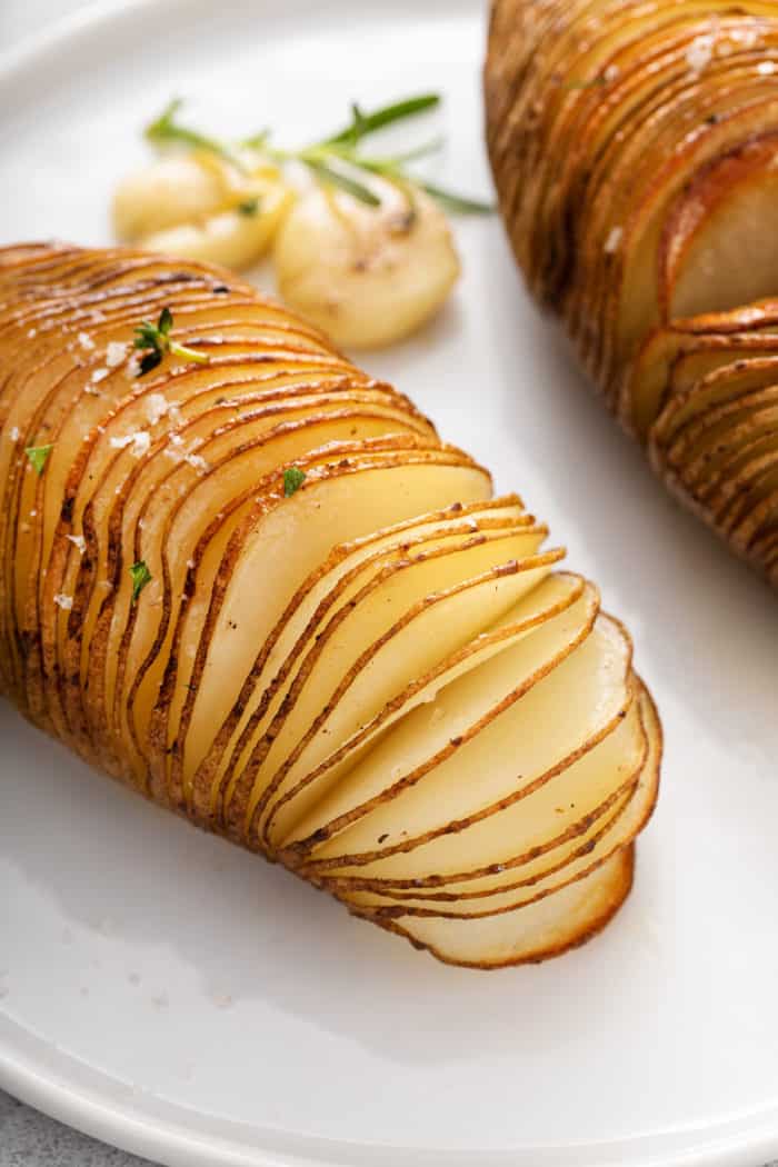 Hasselback potato on a white plate, with the slices fanned apart to show the interior of the potato.