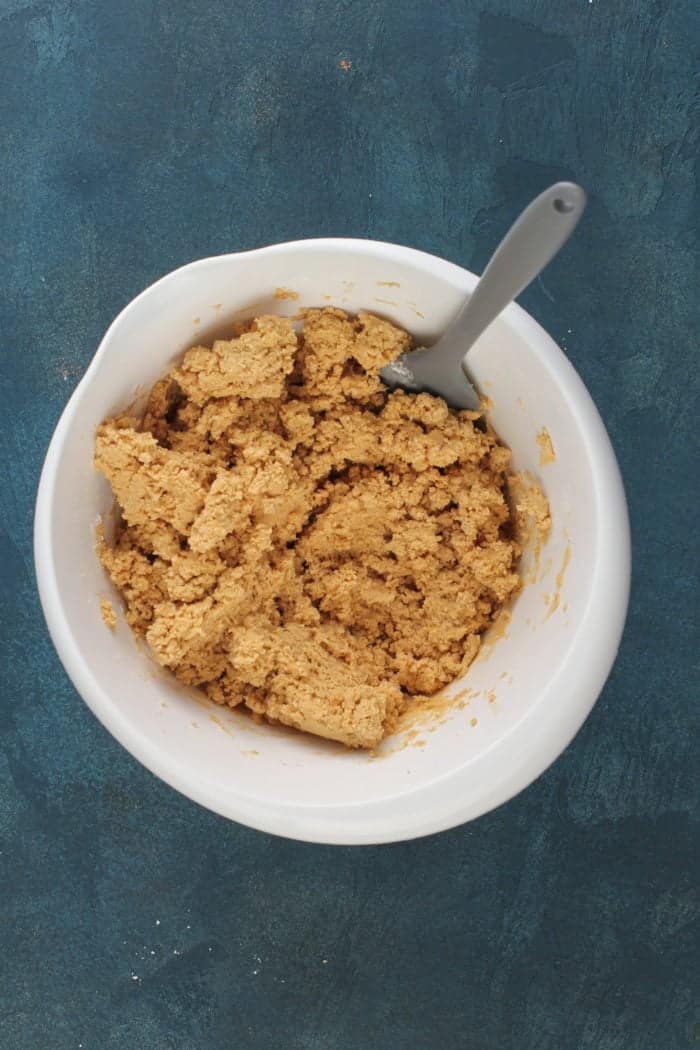 Dough for peanut butter balls being stirred with a spatula in a white mixing bowl.