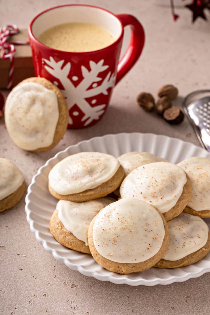 White plate filled with eggnog cookies with a red mug of eggnog in the background.