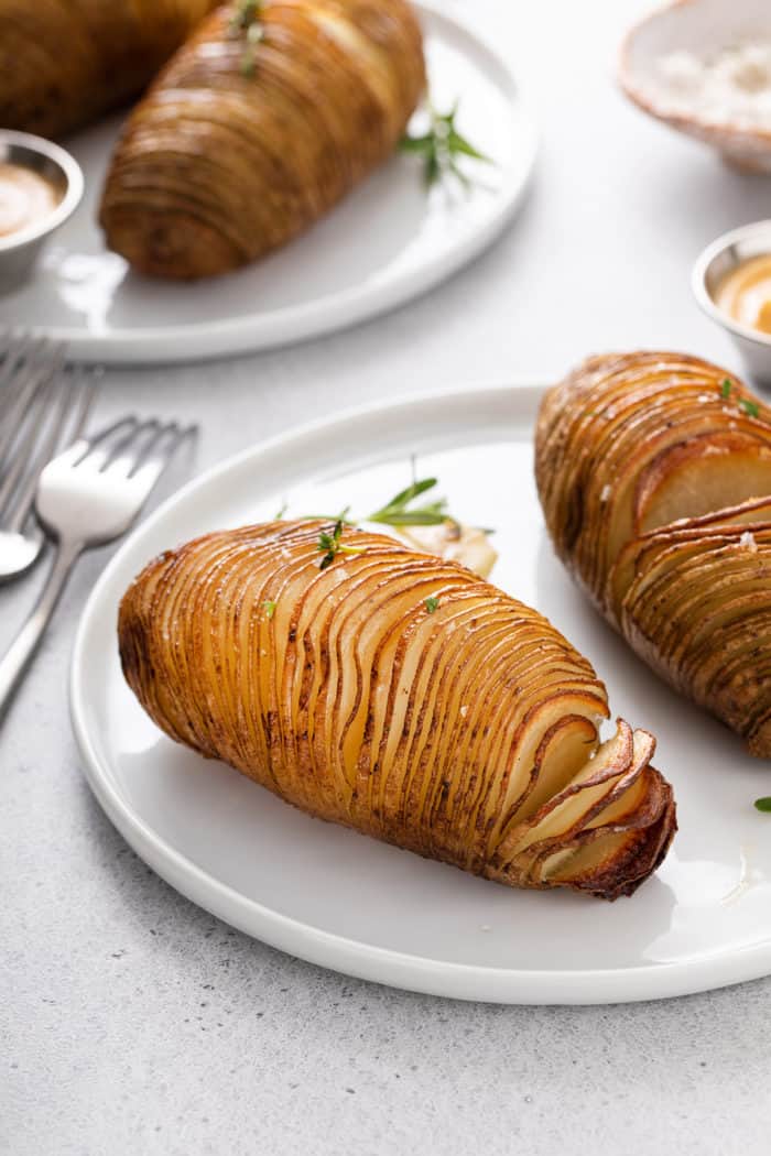 Two roasted hasselback potatoes on a white plate.
