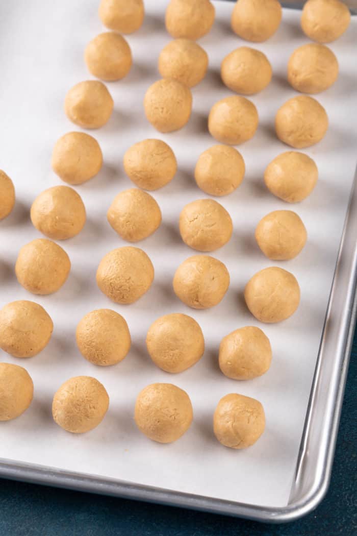 Rolled peanut butter balls on a parchment-lined sheet pan.