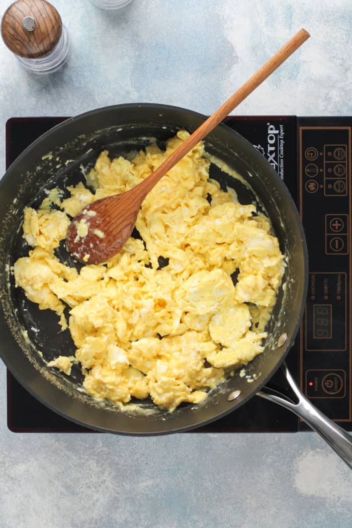 Scrambled eggs being stirred with a wooden spoon in a nonstick pan.