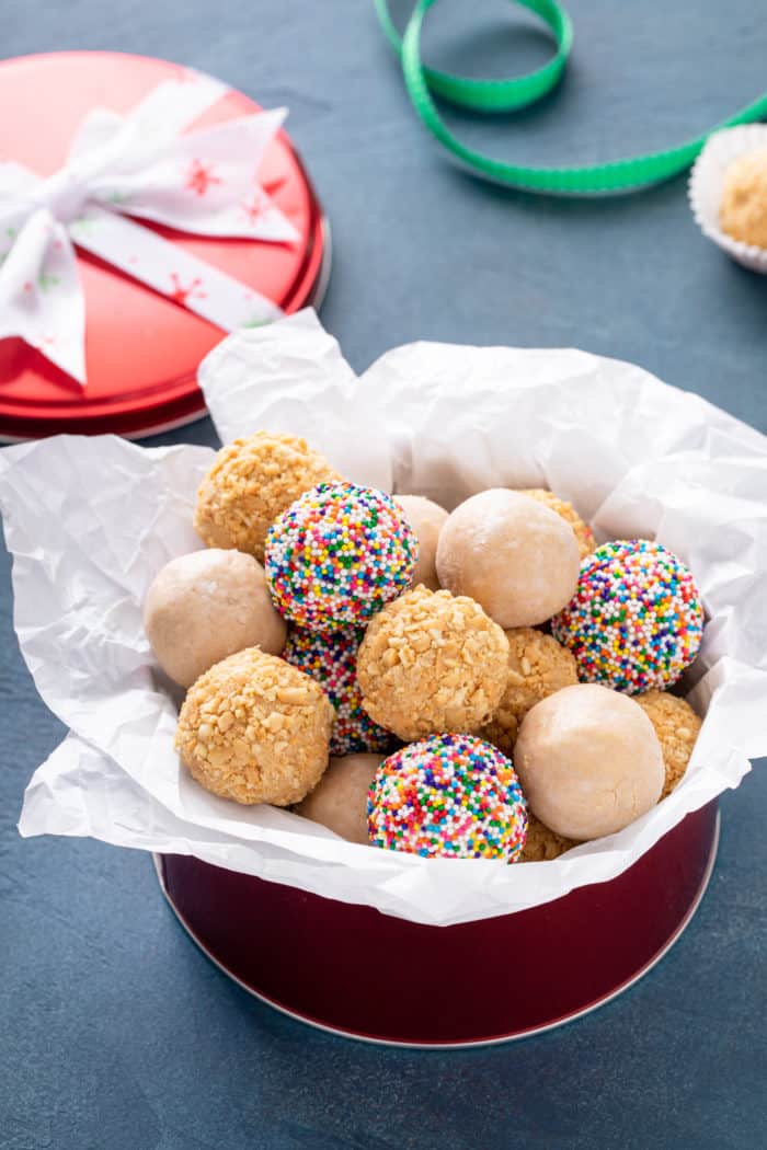 Tissue paper-lined tin filled with peanut butter balls rolled in rainbow nonpareil sprinkles, chopped nuts, and powdered sugar.