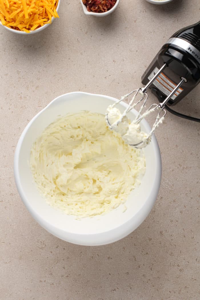 Cream cheese being whipped in a white mixing bowl.