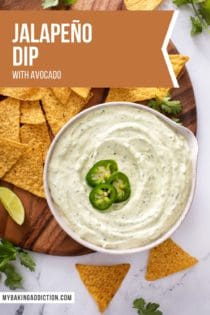 Overhead view of a bowl filled with jalapeño dip next to tortilla chips on a wooden platter. Text overlay includes recipe name.