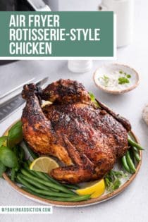 Whole air fryer rotisserie chicken set on a platter with herbs, green beans, and lemon wedges. An air fryer is visible in the background. Text overlay includes recipe name.