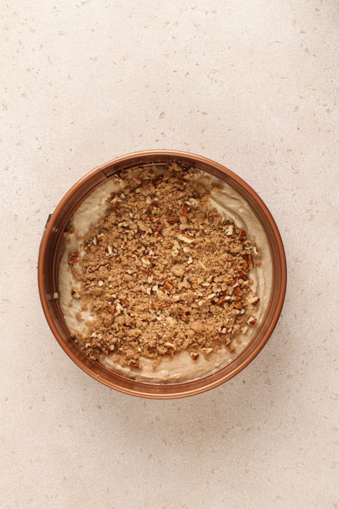 Assembling bisquick coffee cake in a round cake pan, with a layer of cake batter topped with streusel.