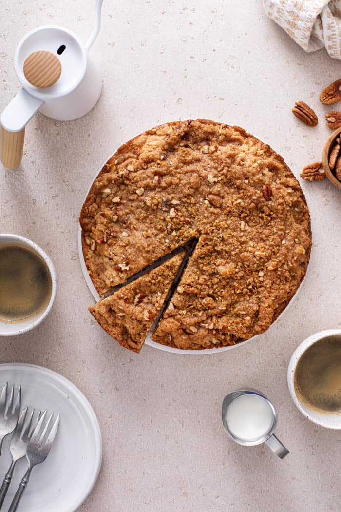 Slice cut from a bisquick coffee cake, set on a beige countertop with cups of coffee.