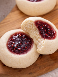 Two thumbprint cookies on a wooden board. One cookie has a bite out of it.