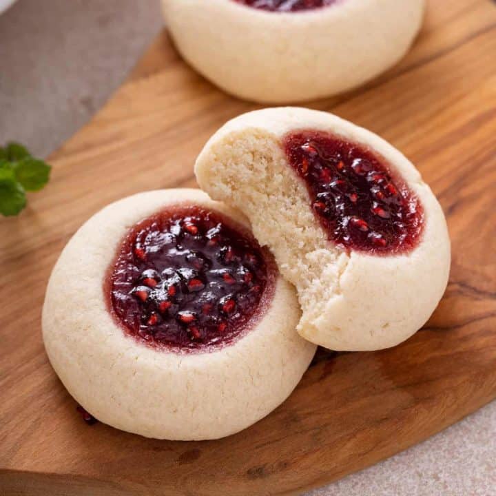 Two thumbprint cookies on a wooden board. One cookie has a bite out of it.