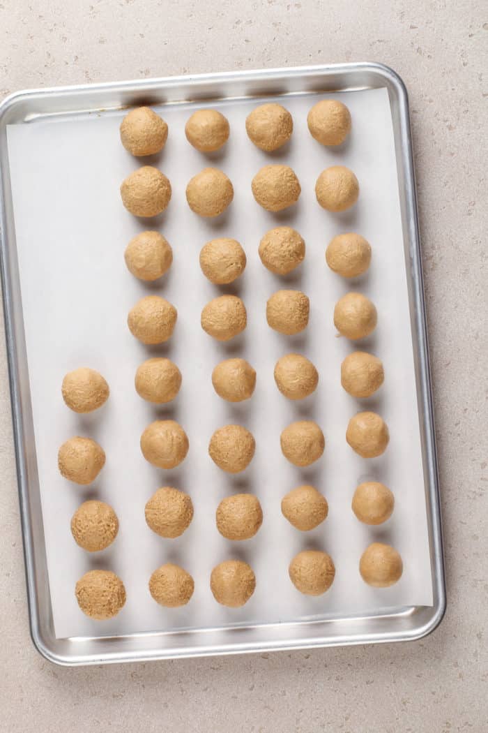 Peanut butter centers for buckeyes lined up on a parchment-lined baking sheet.