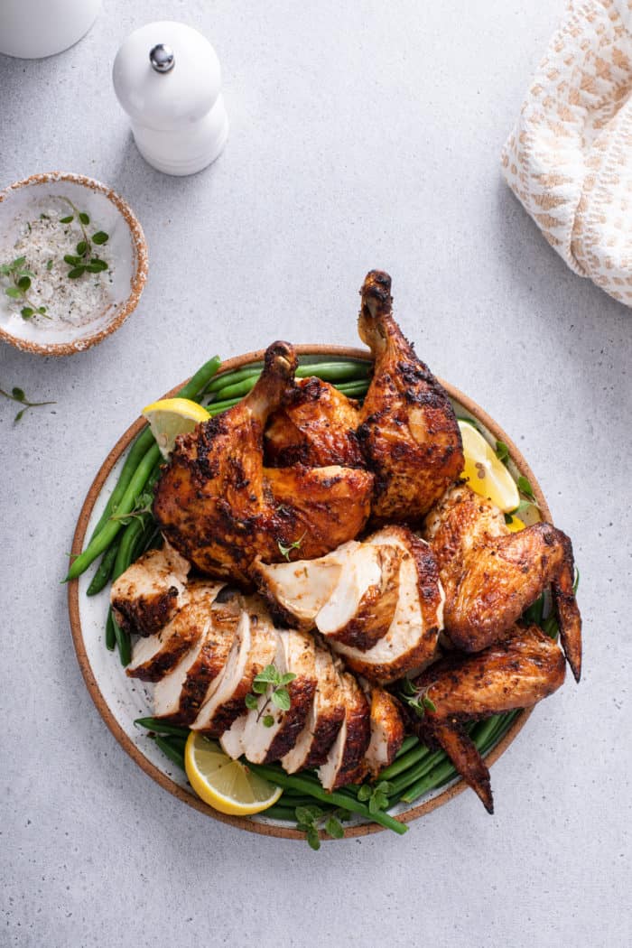 Carved air fryer rotisserie chicken on a platter with green beans and lemon wedges.