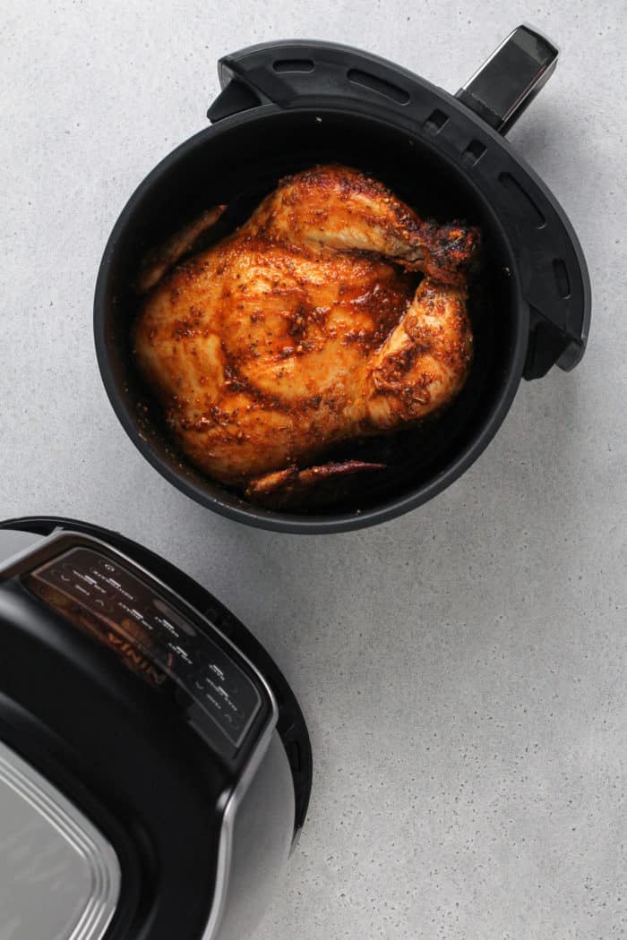 Cooked whole chicken in the basket of an air fryer.