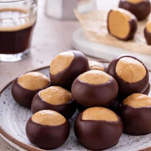 Buckeye candies piled onto a pottery plate. A cup of espresso and more buckeyes are visible in the background.