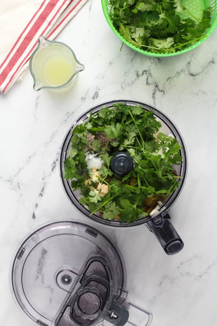 Ingredients for jalapeño dip in the bowl of a food processor on a marble countertop.