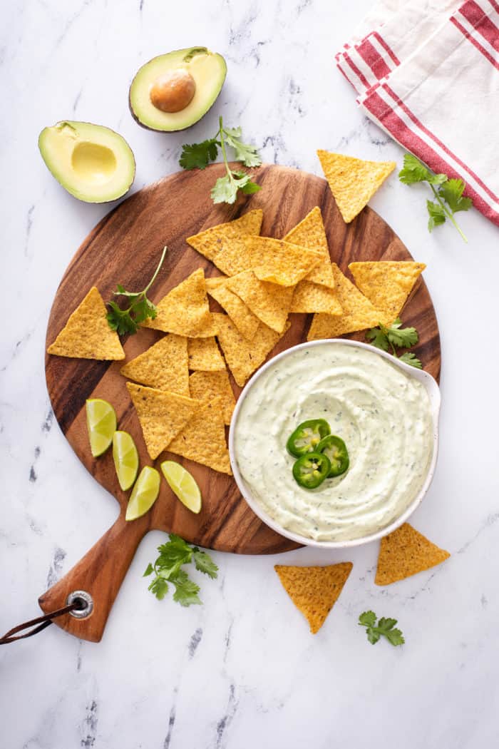 Bowl filled with jalapeño dip on a round wooden board scattered with tortilla chips.