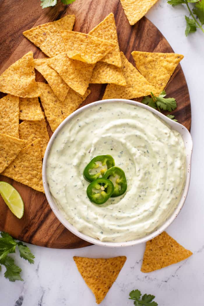Overhead view of a bowl filled with jalapeño dip next to tortilla chips on a wooden platter.