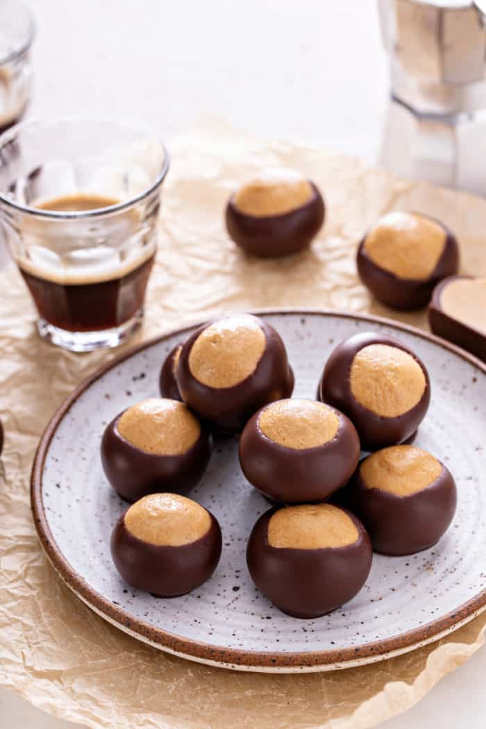 Seven buckeyes on a gray plate, set next to a glass of espresso on a piece of parchment paper.