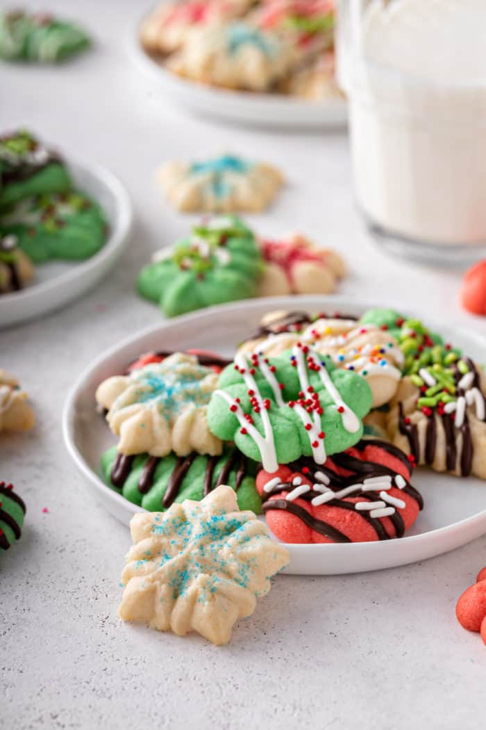 White plate with several spritz cookies. A small snowflake spritz cookie is leaning against the edge of the plate.