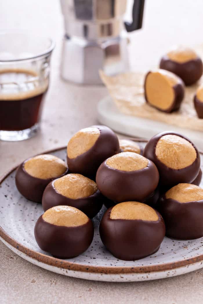 Buckeye candies piled onto a pottery plate. A cup of espresso and more buckeyes are visible in the background.