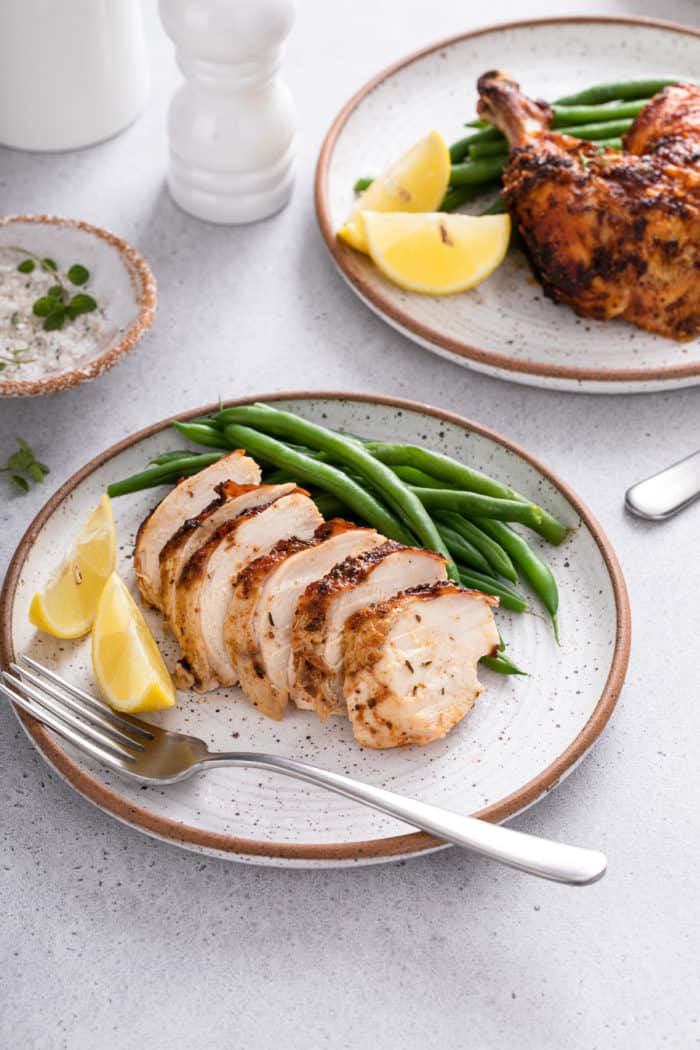 Sliced air fryer rotisserie chicken breast on a plate with green beans and lemon wedges.