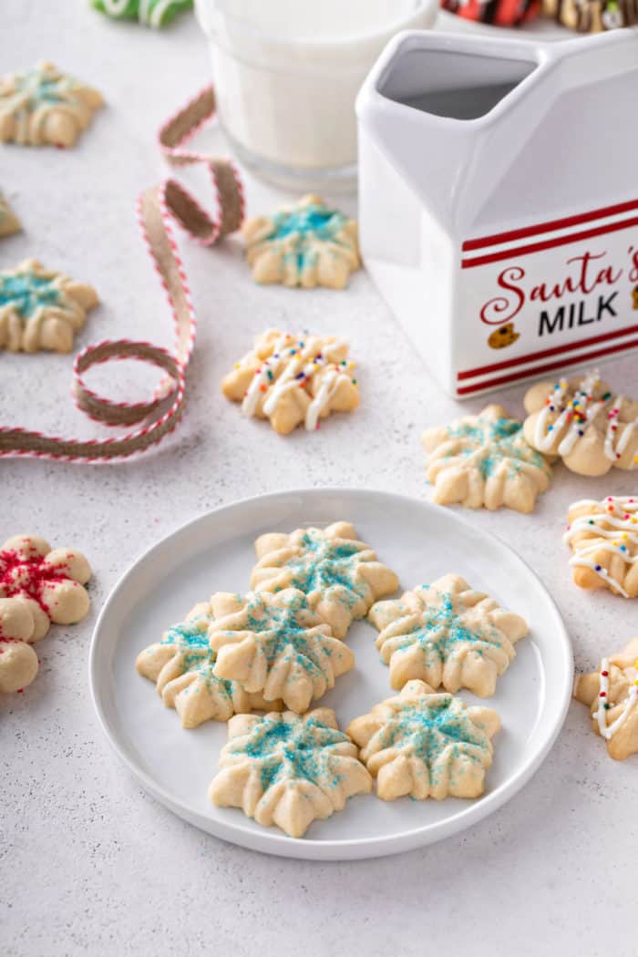 Small snowflake spritz cookies decorated with blue sanding sugar on a white plate.