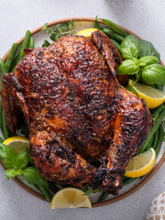 Overhead view of air fryer rotisserie chicken on a platter, garnished with herbs and lemon wedges.