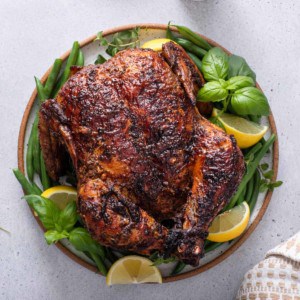 Overhead view of air fryer rotisserie chicken on a platter, garnished with herbs and lemon wedges.