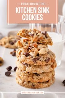 Stack of kitchen sink cookies in front of a glass of milk. The top cookie has been broken in half. Text overlay includes recipe name.