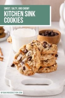 Three kitchen sink cookies stacked in front of a glass of milk. A fourth cookie is leaning against the stack. Text overlay includes recipe name.