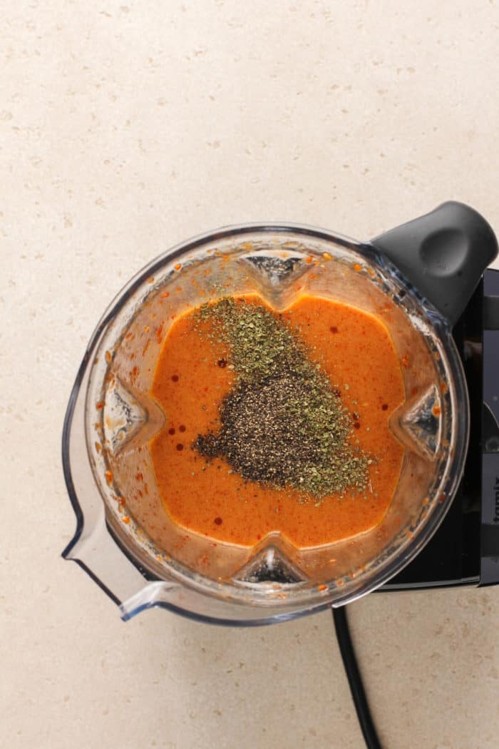 Dried oregano and black pepper being added to chipotle vinaigrette in the jar of a blender.