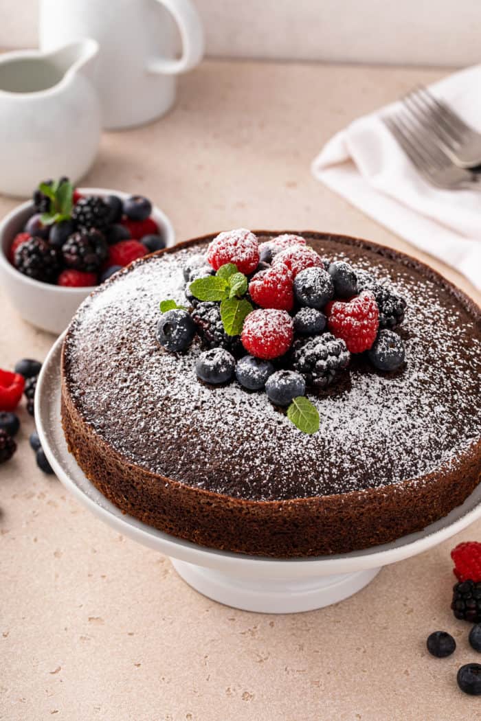 Baked eggless chocolate cake on a cake stand, dusted with powdered sugar and topped with fresh berries.