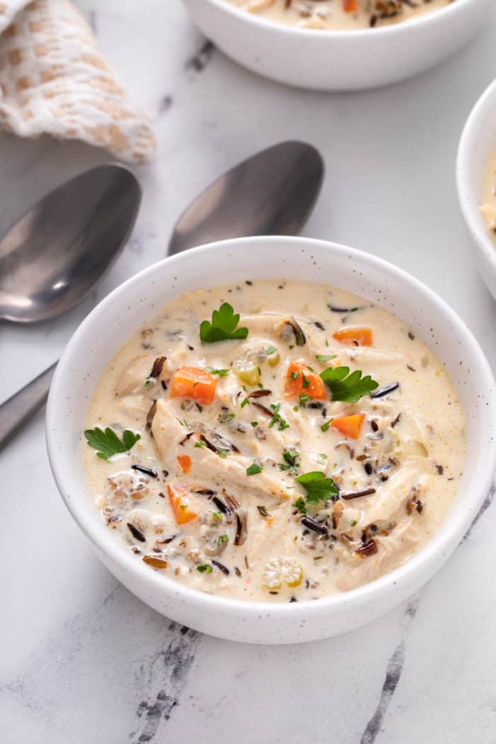 Close up view of chicken and wild rice soup in a white bowl on a marble countertop.