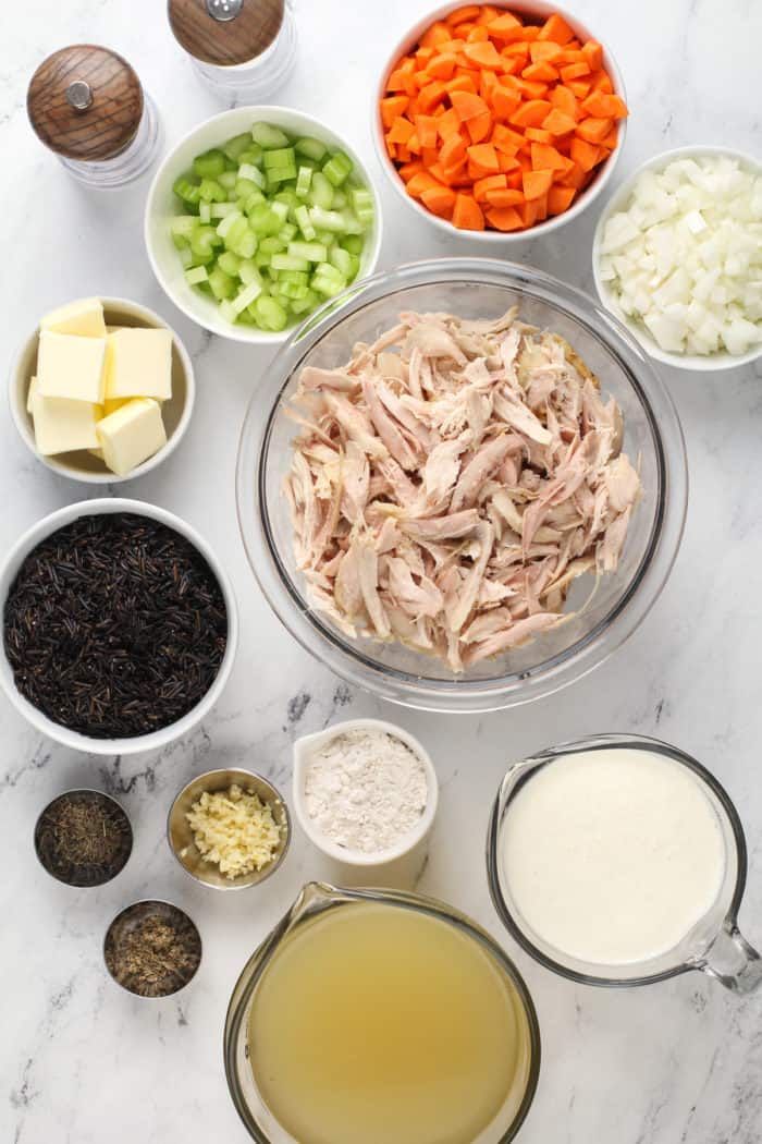 Ingredients for chicken and wild rice soup arranged on a marble countertop.