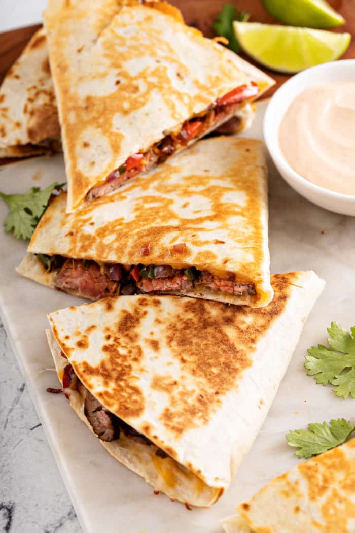 A sliced chipotle quesadilla on a marble board next to a small bowl of dipping sauce.