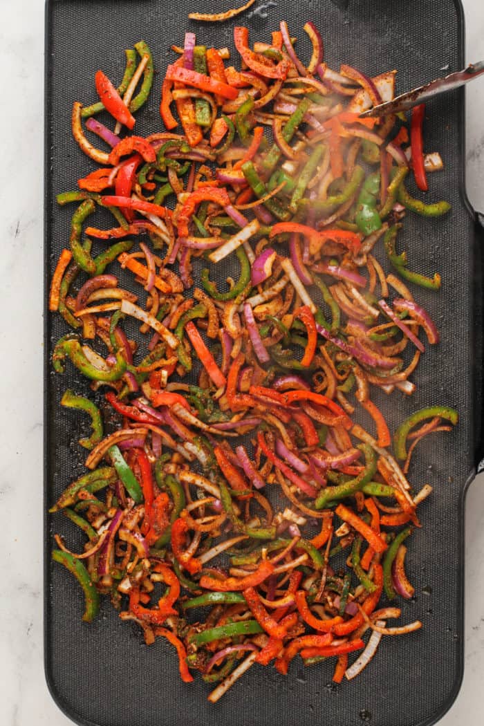 Seasoned fajita veggies cooking on a griddle.