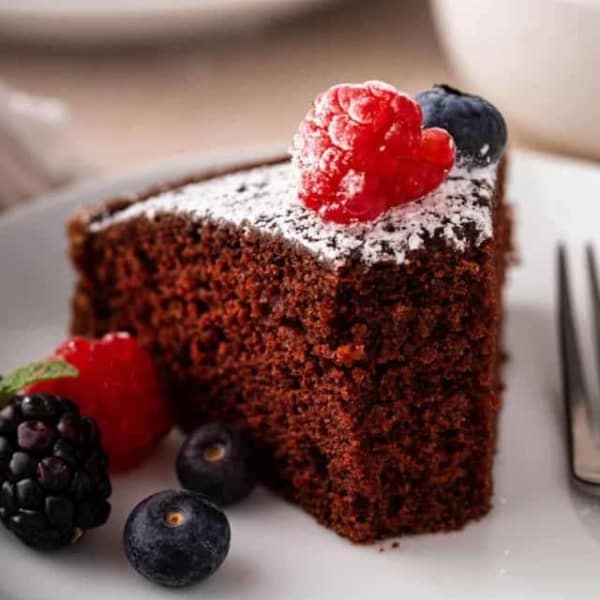 Slice of eggless chocolate cake with several bites taken from it on a white plate.