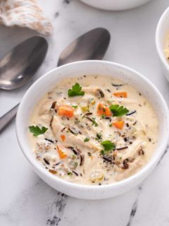 Close up view of chicken and wild rice soup in a white bowl on a marble countertop.
