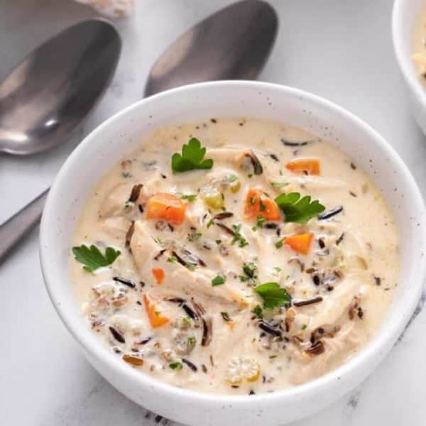 Close up view of chicken and wild rice soup in a white bowl on a marble countertop.