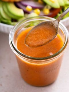 Spoonful of chipotle vinaigrette being held above a jar of the dressing.