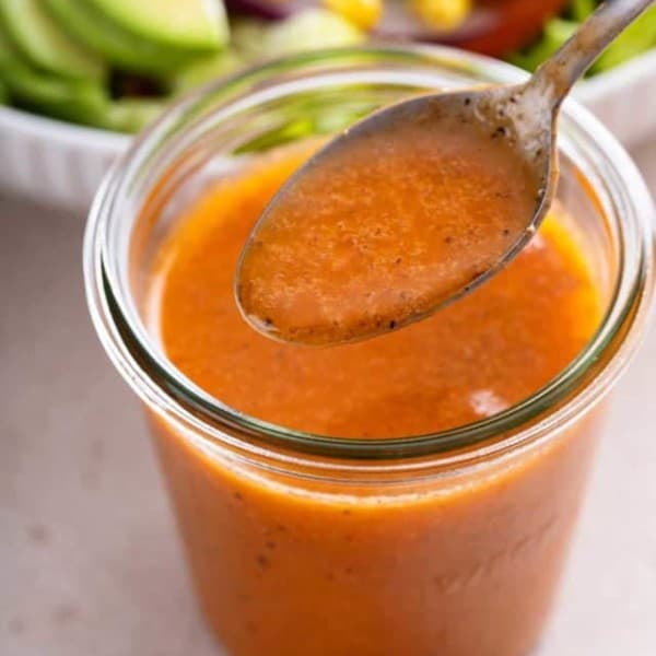 Spoonful of chipotle vinaigrette being held above a jar of the dressing.