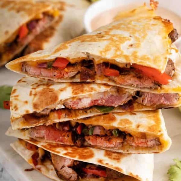 Several slices of chipotle quesadilla stacked on top of each other, with a small bowl of dipping sauce visible in the background.