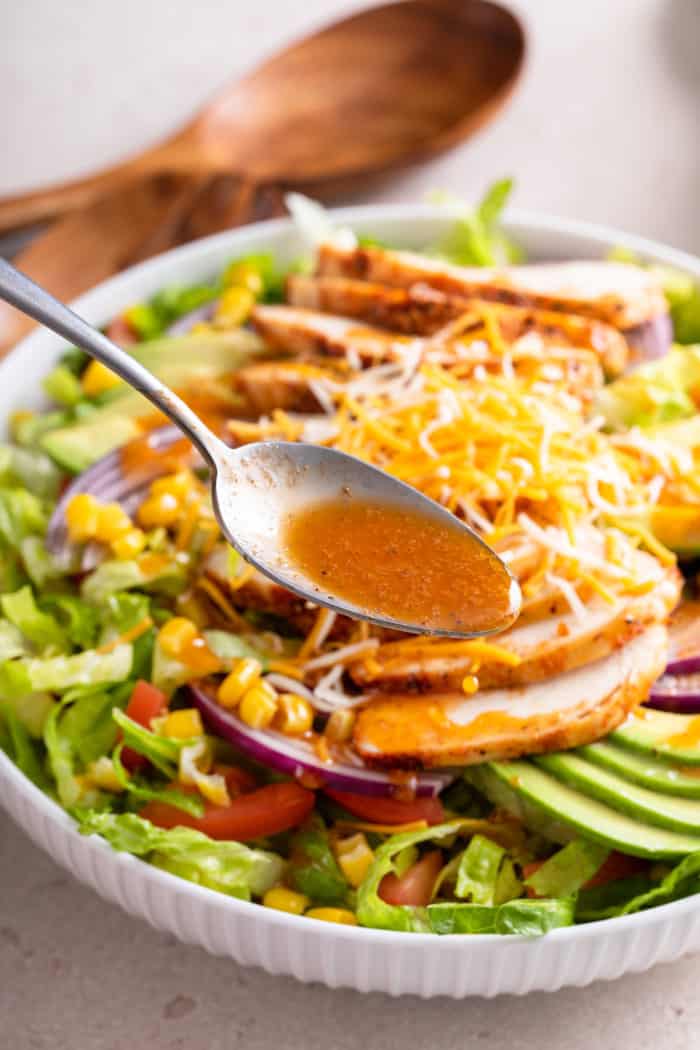 Close up of a spoon adding chipotle vinaigrette over the top of a salad.