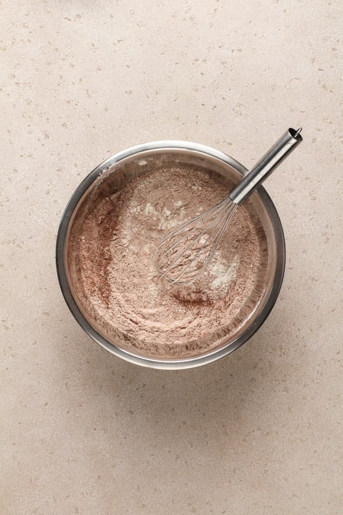 Dry ingredients for eggless chocolate cake whisked together in a metal mixing bowl.