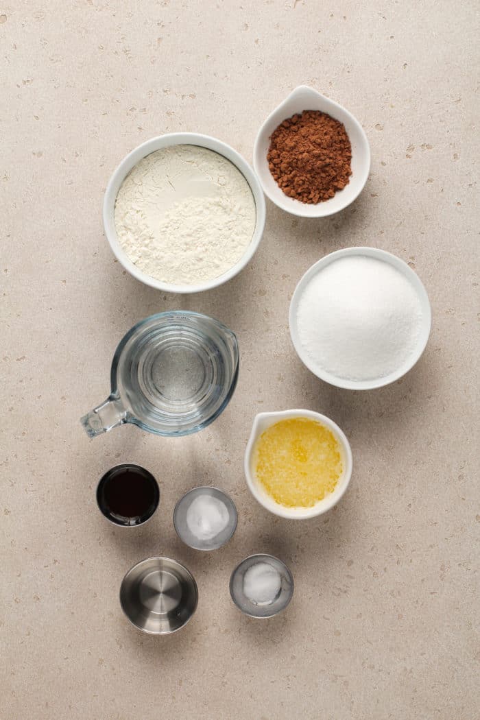 Ingredients for eggless chocolate cake arranged on a beige countertop.