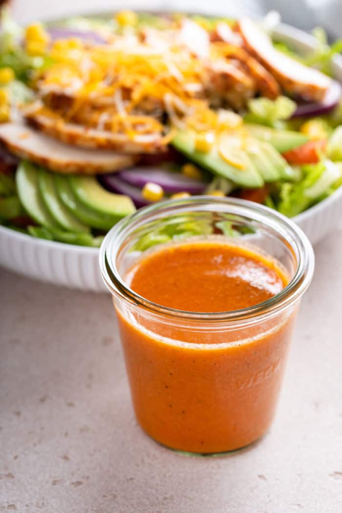 Jar of chipotle vinaigrette set in front of a white bowl of salad.